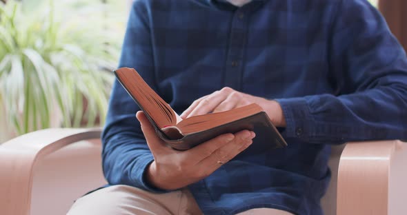 Closeup View of Male Hands Holding Book Young Man is Reading a Book While Sitting in White Chair at