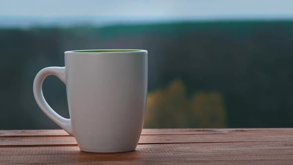 Cup of Hot Tea or Coffee Stands By an Open Window and Emits Steam