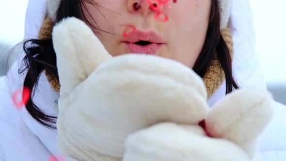 A woman blows red sequins in the shape of hearts from warm fur mittens