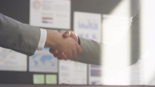 Businessmen Shaking Hands behind Glass Office Wall