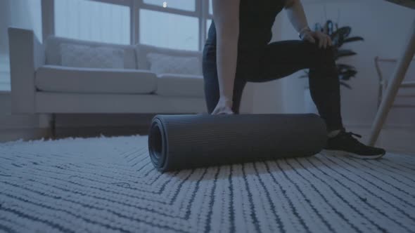 A following shot of a woman rolling out a matt for her at home work outs in her living room. 4k60