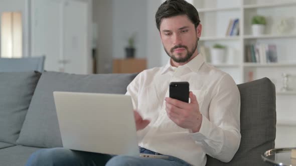 Focused Businessman Working on Smartphone and Laptop at Home