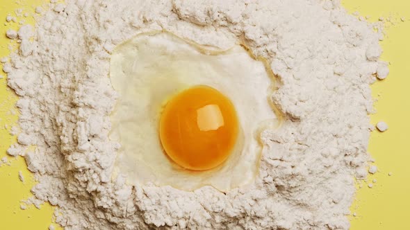 Broken egg yolk on flour for the dough on yellow background