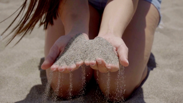 Sand Falling Through Hands Of Woman In Shorts