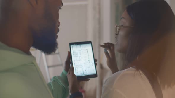 Back View of African Couple Using Apartment Plan on Tablet While Making Renovation Indoor