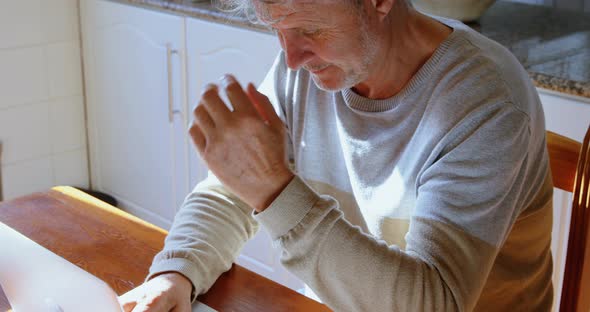 Senior man using laptop in kitchen at home 4k