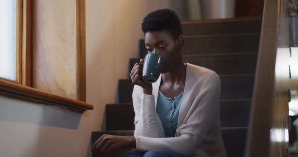 Thoughtful african american attractive woman sitting on stairs an, drinking coffee