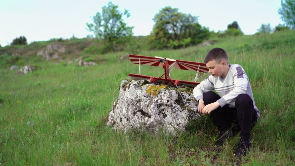 Young Boy Sitting Near Toy Airplane on the Stone and Thinking