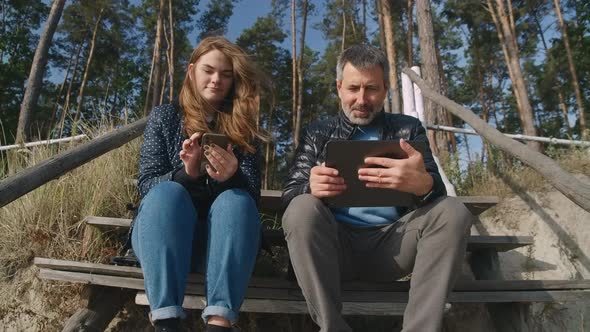 Front View Young Smiling Caucasian Woman Scrolling Smartphone As Positive Mature Man Talking Showing