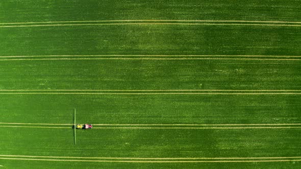 Small tractor spraying the chemicals on the green field, aerial view, Poland