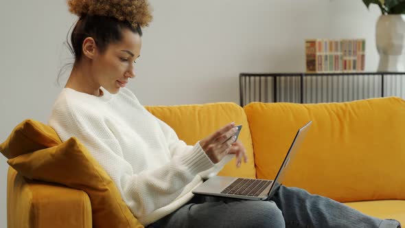 Young AfricanAmerican Woman Holding a Credit Bank Card Entering Payment Information Into an Online