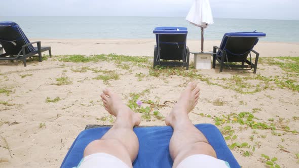 POV to man's legs, feet while relaxing on sunbed near beach in resort in thailand for sun bathing ta