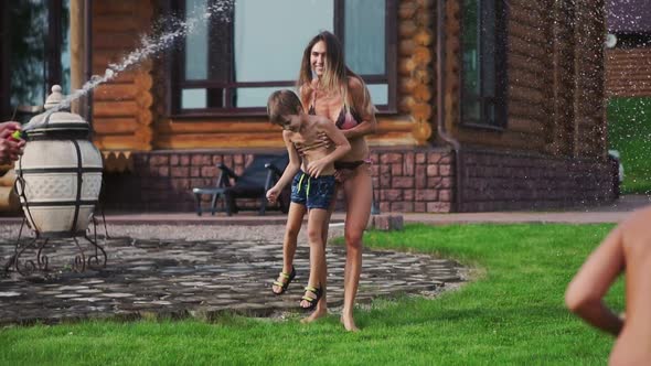 Happy Family with Two Kids Playing with Garden Hose Pouring Water on Grass