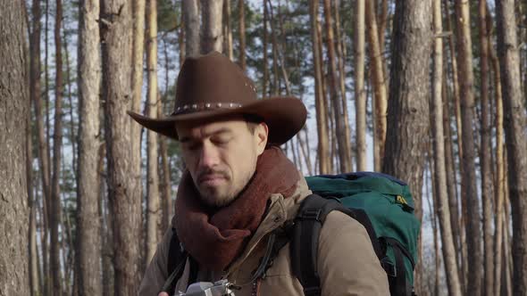 A Man in a Hat Takes Pictures in the Forest