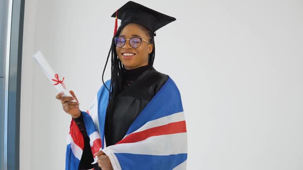 Happy Stylish Afro American Woman Student In Graduate Uniform Shows Diploma and Smiling with British