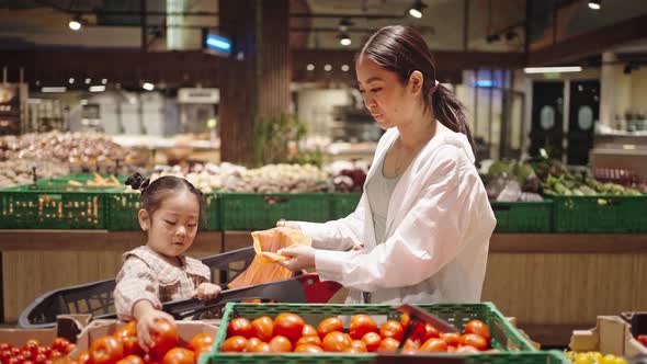 Daughter Puts Tomatoes Into Orange Bag Sitting in Cart