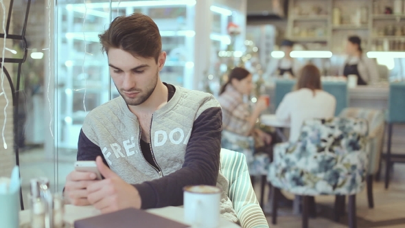 Young Man With Smartphone Sitting In Cafe