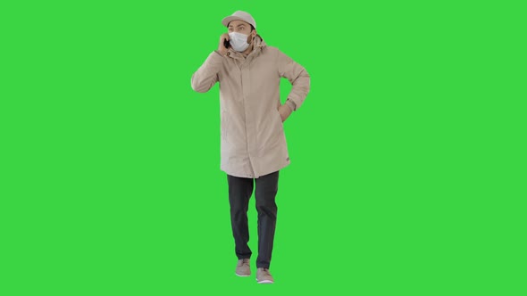 Casual Man in Outdoor Clothes and Medical Mask Walking and Talking on the Phone on a Green Screen