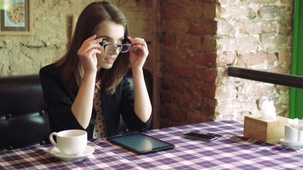 Business Lady In Glasses Drinking Coffee, Using a Tablet And Smiling In Cafe 