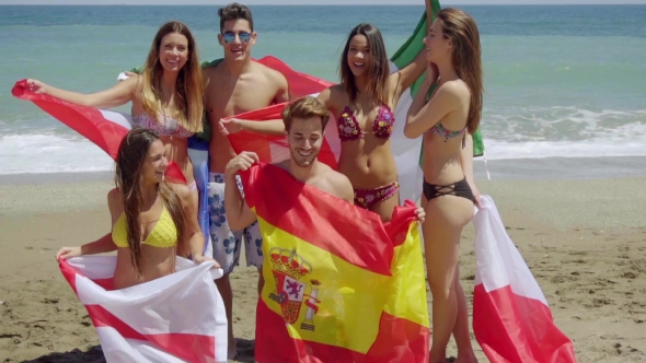 Group Of Friends In Swim Suits With Flags At Beach