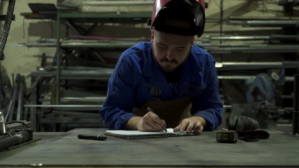 Concentrated mechanic in workshop writing notes in notepad