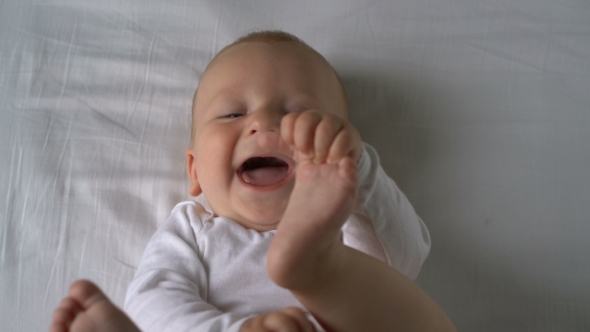 Mother Tickles The Baby And He Laughs Lying On The Bed