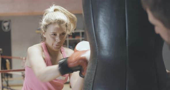 Confident Blond Caucasian Woman Boxing Punching Bag in Sports Club. Portrait of Concentrated Female alt