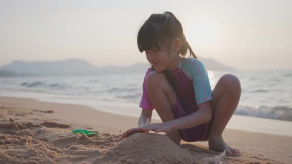 Asian little girl playing sand on beach with sea, kid feeling enjoy and fun to make her own castle.
