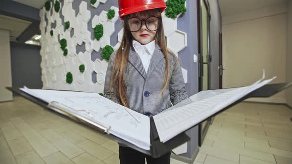 Young Girl in Striped Shirt Wearing Large Glasses and Holding Black Binder While Standing in Front