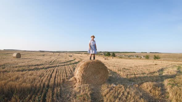 Little Girl in a Field with Hay Jump at Sunset. Girl Near a Hay Bale in the Countryside