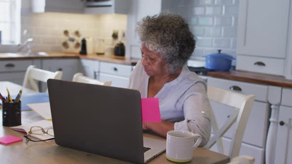 Senior african american woman sticking memo notes on her laptop at home