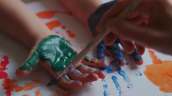 Mom Paints Children's Hands with Colored Paints