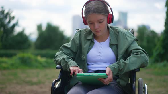 Medium Shot Portrait Sad Teenage Disabled Caucasian Girl in Wheelchair Listening to Music in