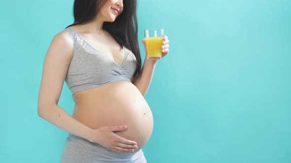 Young Pregnant Woman with Big Belly Holding a Glass of Juice