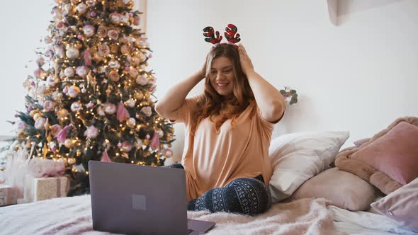 Young Plus Size Woman Talking with Family Via Video Call on Laptop Sitting at Home Near Christmas