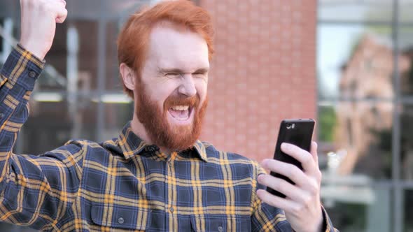 Outdoor Redhead Man Excited for Success on Smartphone