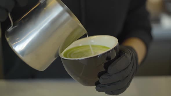 Unrecognizable Bartender Adding Milk To Matcha Green Tea. Close-up of Hands in Protective Black