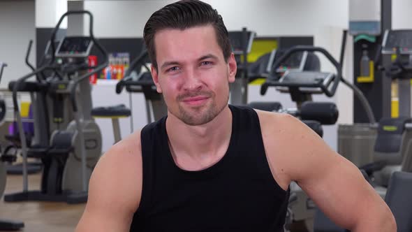 A Young Fit Man Points at the Camera and Nods with a Smile in a Gym - Closeup