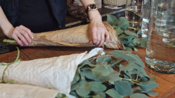 Woman Florist Wraps Something In a Sheet Of Parchment And Bandaging Tape