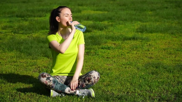 Running Woman Stopped To Drink Water In The Park. Fitness Girl Training Outdoors