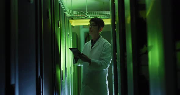 Asian male it technician in lab coat using tablet checking computer server