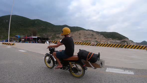 Tracking shot of male person with flip flops driving on motorbike along coastline of Vietnam.