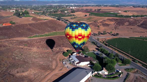 A hot air balloon rises over the California wine country landscape - aerial drone footage with dynam