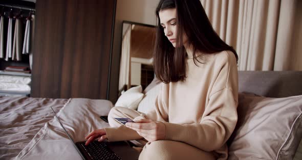 Young Woman Holding Credit Card Making Online Payment on Laptop at Modern Home