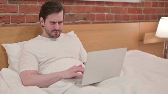 Casual Young Man Reacting to Loss on Laptop in Bed
