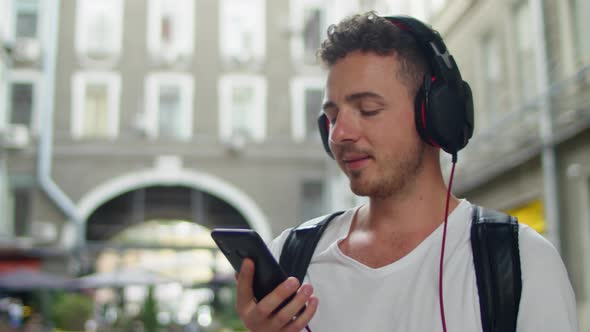 Smiling Handsome Young Man Listening Music From His Smartphone in Red Headphones Dancing on Street