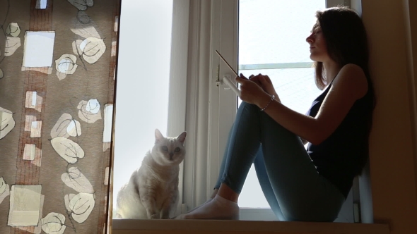 Young Beautiful Woman With Tablet And Cat On The Window-sill
