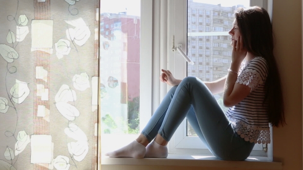 Young Beautiful Woman With Smartphone On The Window-sill