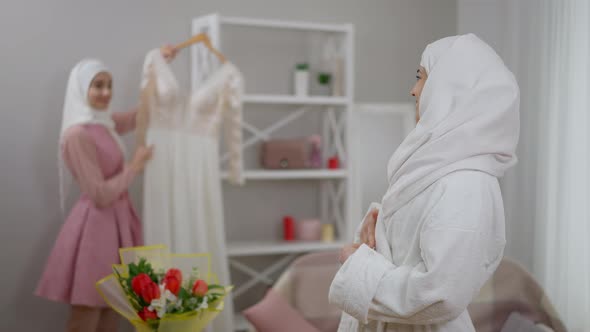 Portrait of Gorgeous Middle Eastern Bride in White Hijab Looking Back at Bridesmaid Showing Wedding