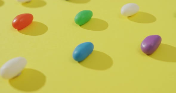 Video of close up of rows of multi coloured sweets over yellow background